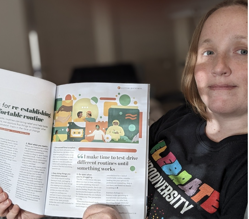 Rosemary Richings in a black celebrate neurodiversity shirt. Her hair is in a loose ponytail and she has blue eyes and reddish blonde hair. She is holding up a copy of a magazine she wrote for and wearing black and white checkered leggings. There is a gold wedding ring on her hand.